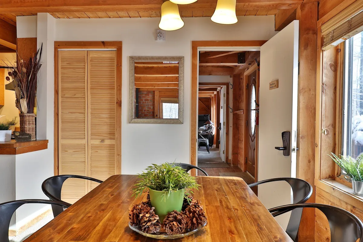 A warm dining space with a wooden dining table, green plant centerpiece, decorative mirror, light fixtures, and open doorways leading into other areas. The setup is perfect for family dinners or celebratory events, with ample seating for groups.