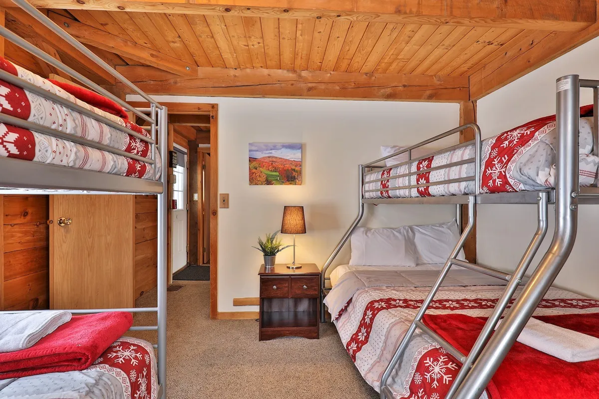 A welcoming bunk room with multiple stacked bunk beds, a nightstand with a glowing lamp, and cheerful decorative wall art. The ambiance is playful yet peaceful, ideal for children, siblings, or friends to share stories or unwind after a day of adventure.