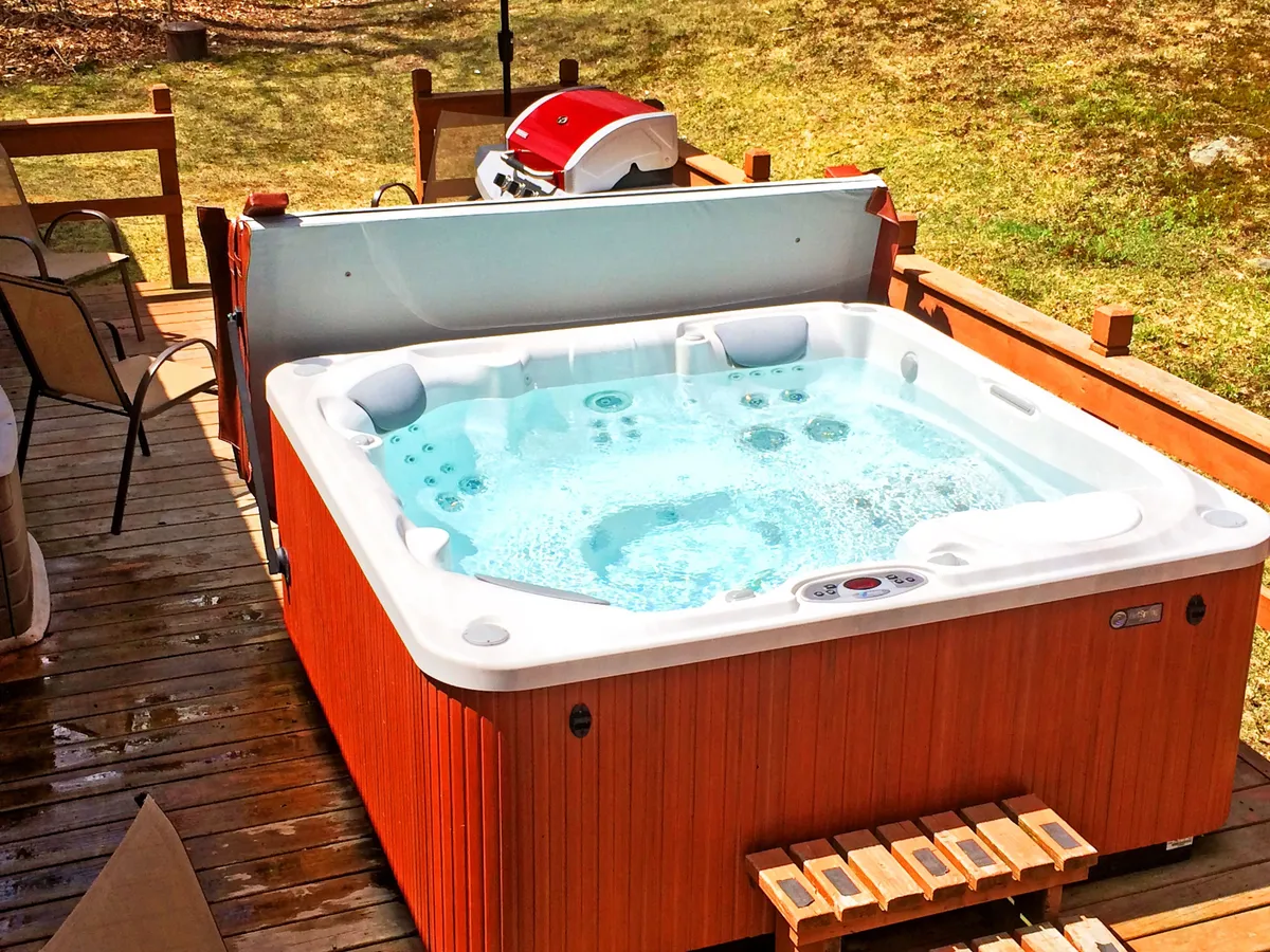 This exterior shot features a spacious wooden deck equipped with a hot tub and a grill. The deck is surrounded by lush greenery and offers ample room for socializing or relaxing. The hot tub is prominently positioned, inviting guests for an après-ski soak or starlit relaxation. The grill hints at the potential for summer BBQs and outdoor gatherings.