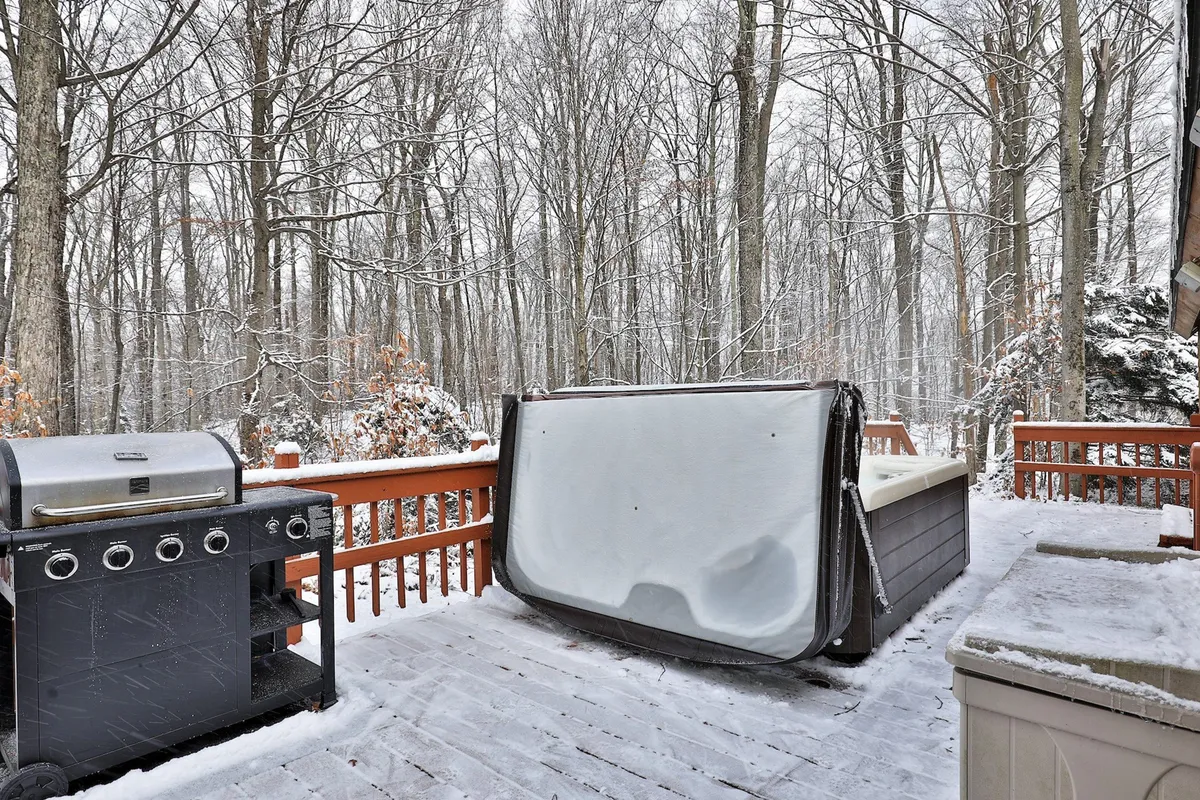 An inviting exterior shot of a wooden deck surrounded by trees, featuring a grill and a hot tub. The deck reflects both relaxation and outdoor entertaining, with ample space for families to unwind after a day of activities.