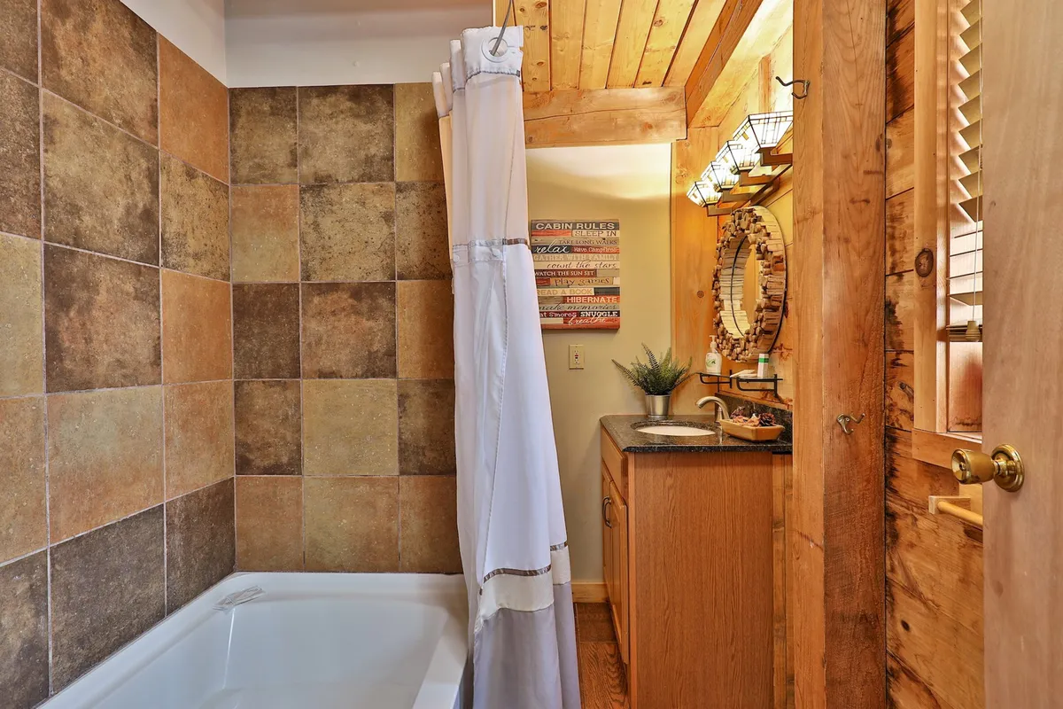 A modern, well-kept bathroom with a deep bathtub, stylish sink, large mirror, and decorative wall art. The inviting lighting and rustic accents create a tranquil atmosphere, perfect for unwinding after a day outdoors.