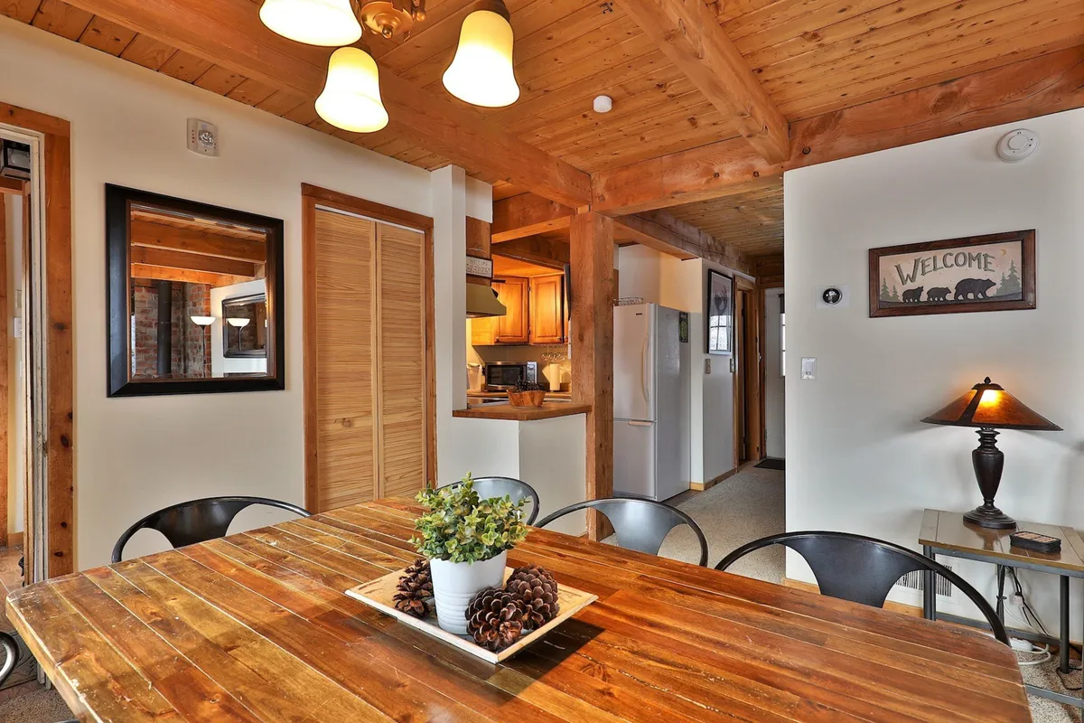 A cozy dining area centered on a wooden dining table, surrounded by inviting decor such as a welcome sign, potted plant, and hanging light fixtures. The setup is ideal for family dining, social gatherings, and intimate meals.